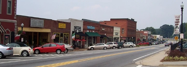 Downtown street lined with brick storefronts, parked cars, and a wide road.