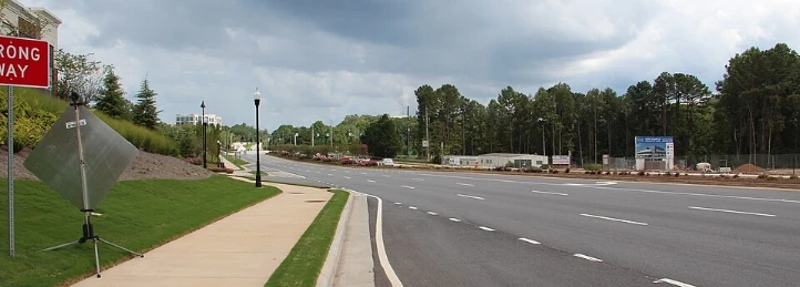 Wide suburban road with sidewalk, construction site, trees, and stormy sky.