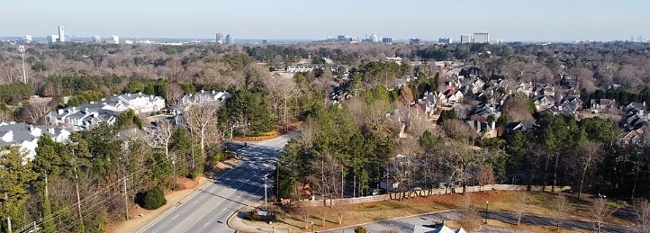 Aerial view of a suburban neighborhood with tree-lined roads and distant city skyline.