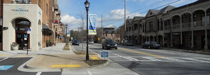 Downtown Austell street with storefronts, crosswalk, cars, and town banner.