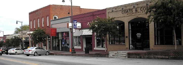 Historic downtown main street with brick storefronts, parked cars, and local shops along a tree-lined street.