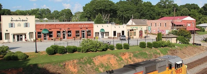 Downtown storefronts overlooking railroad tracks with brick buildings, landscaped greenery, and small-town streetscape