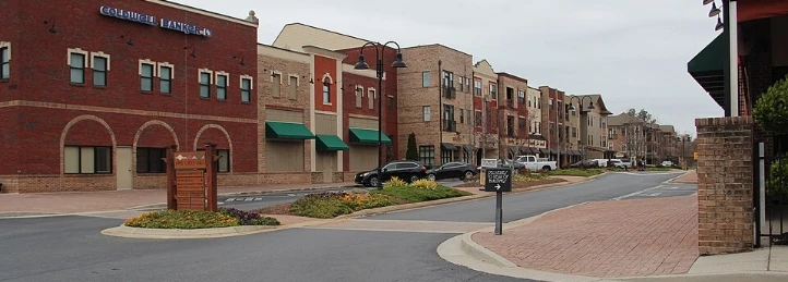 Mixed-use downtown street with brick buildings, apartments, storefronts, and landscaped sidewalks in a modern urban district.