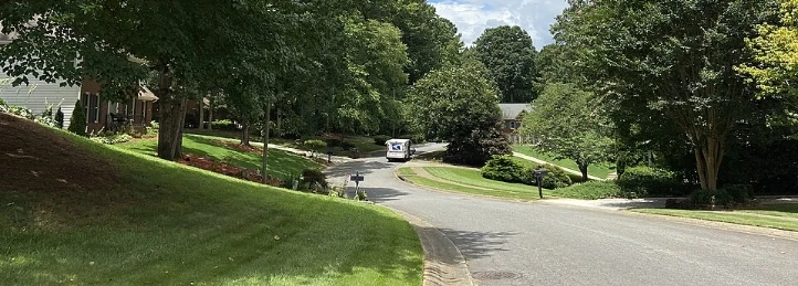Quiet residential street with green lawns, trees, mailboxes, and a white van.