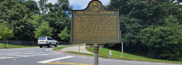 Sandy Springs historical marker beside a tree-lined road and sidewalk.