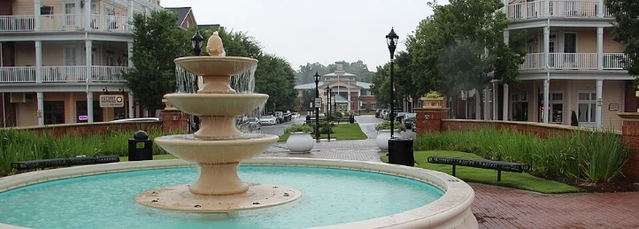 Town center fountain with brick walkways, benches, lampposts, and residential buildings.