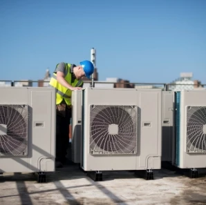 HVAC technician servicing rooftop condenser units under a clear blue sky.
