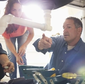 Plumber explaining under-sink pipe repair to a homeowner.
